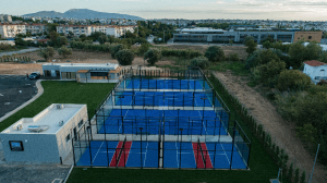 This image showcases a state-of-the-art padel court complex featuring six meticulously constructed standard padel courts. The courts are arranged in two parallel rows of three, with vibrant blue synthetic turf and precision-marked white lines, creating a visually striking and professional playing surface. Red central walkways provide clear player access, enhancing both functionality and aesthetic appeal. Each court is enclosed with high-strength steel structures and tempered glass walls, ensuring optimal durability and player safety. Integrated LED lighting systems are mounted on robust poles, ensuring high visibility for evening matches and tournaments.